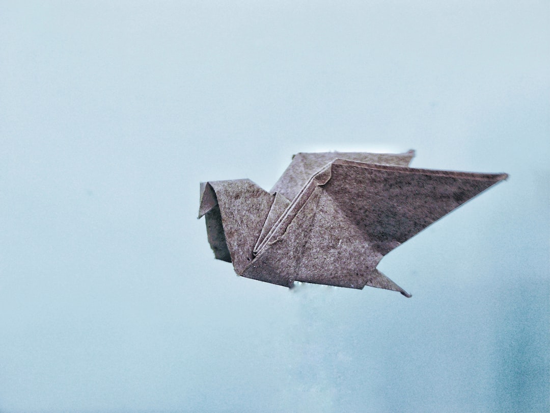 A repeating pattern of origami animals arranged in a diamond symmetry on a textured background. Elements include cranes, foxes, and other folded creatures. — base photo: A textured concrete building facade with a subtle interplay of brown and white tones, providing a ne