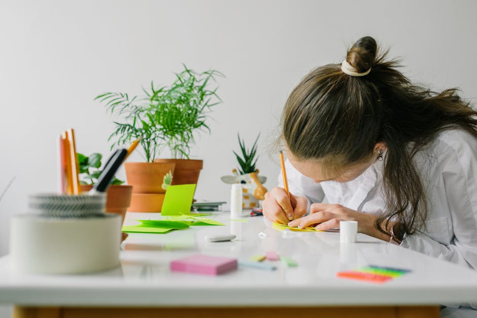 Seamless mirror wallpaper pattern — Origami by wallpaper⁶ — base photo: A woman with a bun writes at a desk surrounded by plants and stationery.