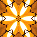 Close-up of a kaleidoscope pattern made from stained glass fragments, illuminated by warm backlighting. Features geometric shapes and cracked glass details.