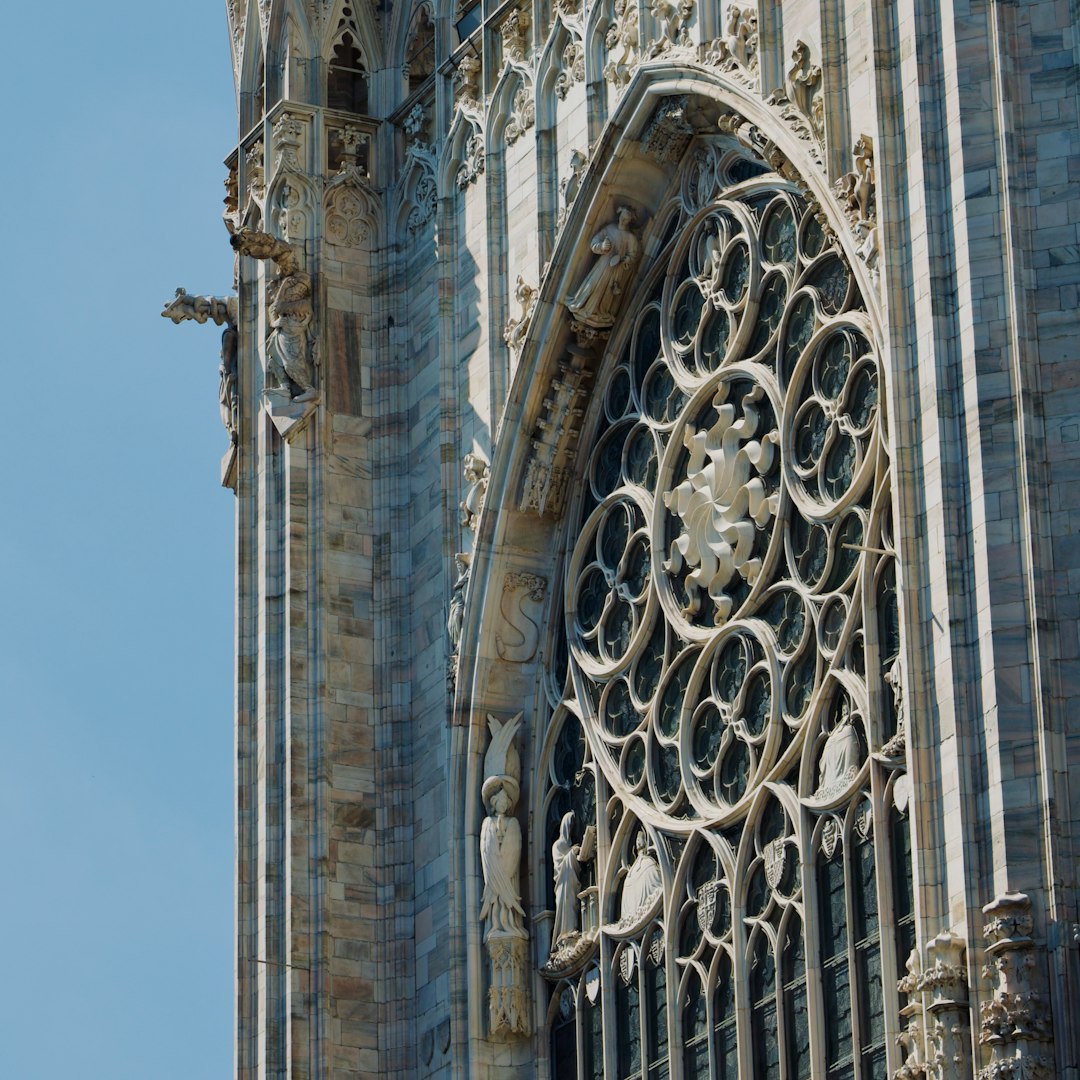 A seamless wallpaper pattern featuring rotating Gothic rose window segments in a pinwheel symmetry, showing intricate stone and glass. — base photo: A high-detail photograph by Garvit Nama capturing the intricate stone tracery and vibrant glass of a