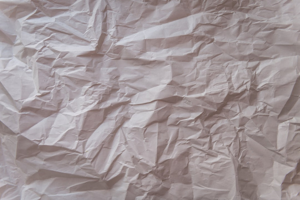 Crinkled paper texture repeating in a mirror symmetry pattern, showcasing the subtle details of paper folds and shadows. — base photo: A close-up, macro shot of crinkled paper, showcasing the detailed textures and deep shadows formed b