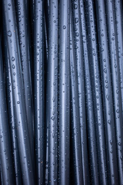 Abstract wallpaper pattern inspired by wet folding origami, featuring dark, vertically arranged elements with a mirror symmetry repeat. From Monstera Production. — base photo: An abstract close-up view of vertically aligned, dark, wet pipes with glistening raindrops clinging 
