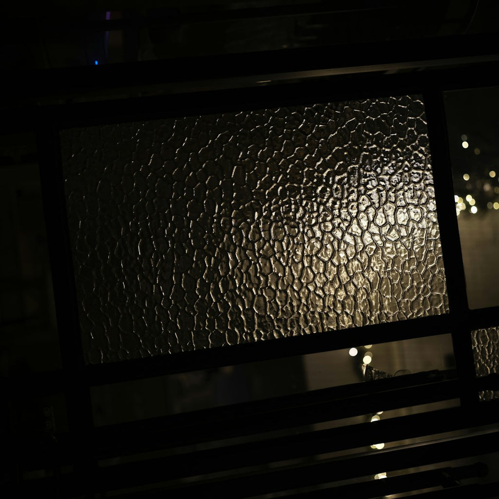 A seamless diamond-shaped repeating pattern of textured amber and dark stained glass with a glowing architectural feel. — base photo: A close-up shot by Yunshuo Qu capturing the intricate texture of a stained glass window reflecting w