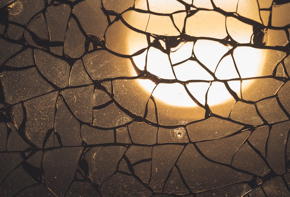 Close-up of a kaleidoscope pattern made from stained glass fragments, illuminated by warm backlighting. Features geometric shapes and cracked glass details. — base photo: A close-up view of a cracked stained glass pattern, dramatically lit from behind. The backlighting h
