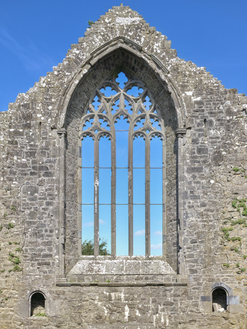 Gothic Arches Kaleidoscope wallpaper pattern inspired by Gothic tracery, featuring repeating pointed arches and geometric symmetry. — base photo: A detailed view of Gothic tracery from Clontuskert Augustinian Friary. The image captures the delica