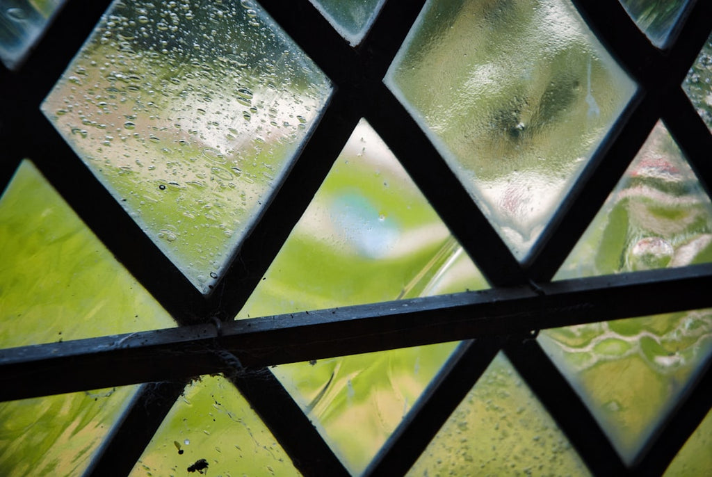 Diamond-shaped leaded glass panes arranged in a symmetrical kaleidoscope pattern with a blurred green background. — base photo: A close-up view reveals the detailed craftsmanship of diamond-shaped leaded glass panes. Beyond the 