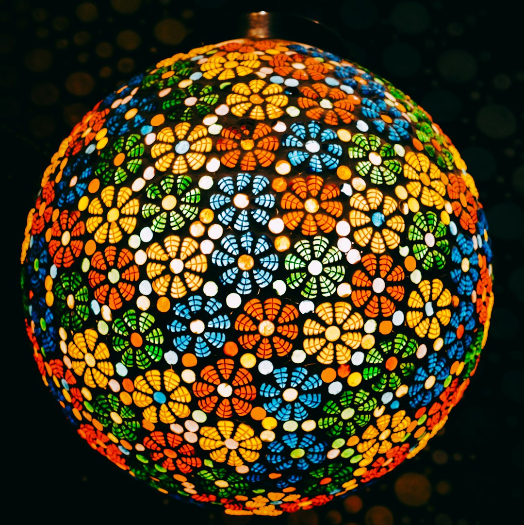 A colorful stained glass mosaic pattern arranged in a repeating diamond symmetry, featuring vibrant blue, red, and yellow shards. — base photo: A high-resolution photograph by Garv Chaplot capturing a multicolored glass ball with intricate mosa