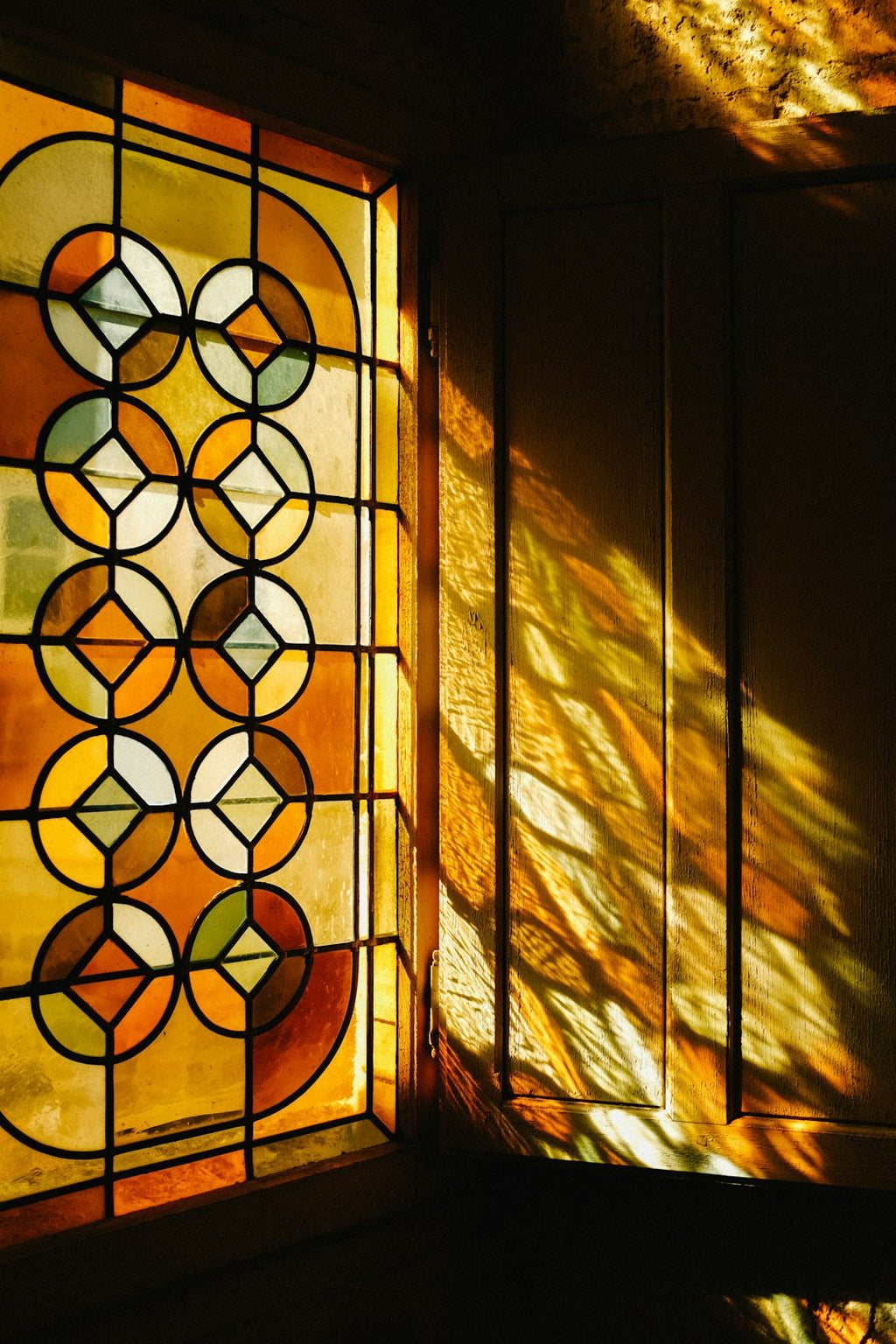 A vibrant, geometric kaleidoscope pattern made of stained glass shards, with dark "lead" lines forming intricate symmetrical shapes on a wall. — base photo: A close-up view of an ornate leaded glass window, showcasing the sharp lines of the metal "leads" se