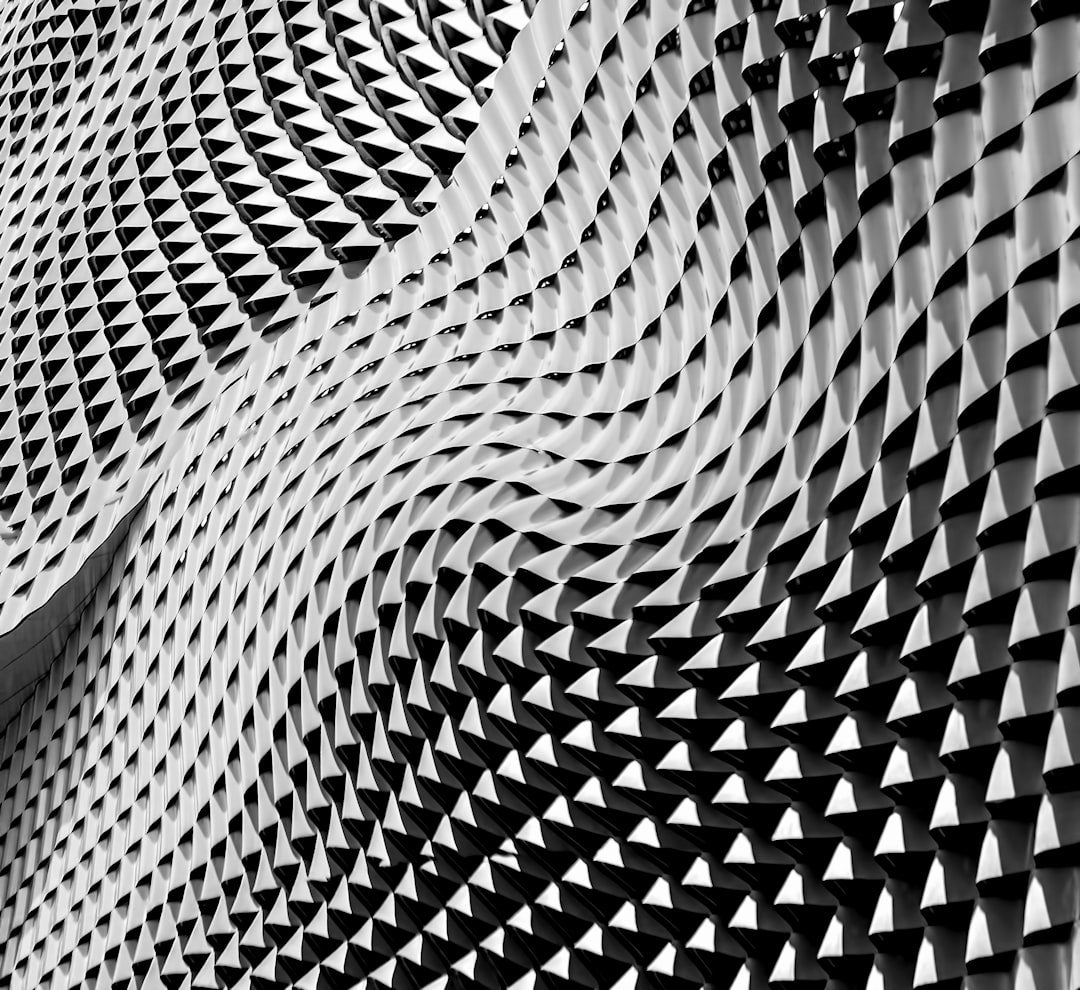 A seamless monochrome op-art pattern featuring mirrored geometric shards and sharp angular transitions in black and grey. — base photo: A stark, high-contrast photograph of angled obsidian-colored planes and light-gray gradients arrange