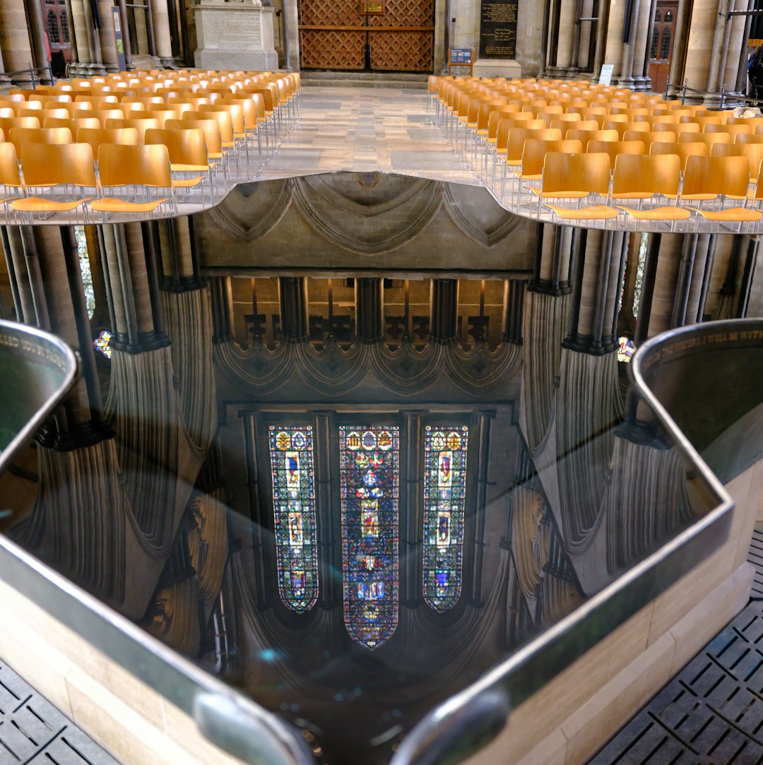 A repeating pinwheel pattern of distorted stained glass colors in shades of blue, green, and gold with a watery texture. — base photo: A high-contrast photograph of sunlight streaming through stained glass windows, captured as a shimme