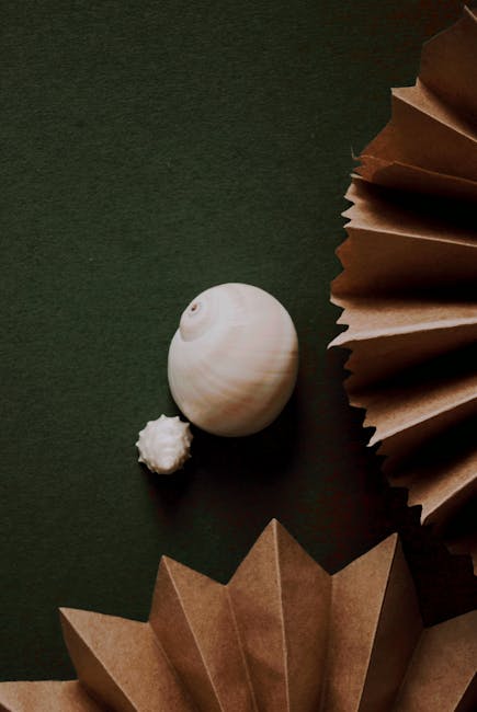 Seamless kaleidoscope wallpaper pattern — Origami by wallpaper⁶ — base photo: Seashells and folded paper create an artistic flatlay on a green textured surface.