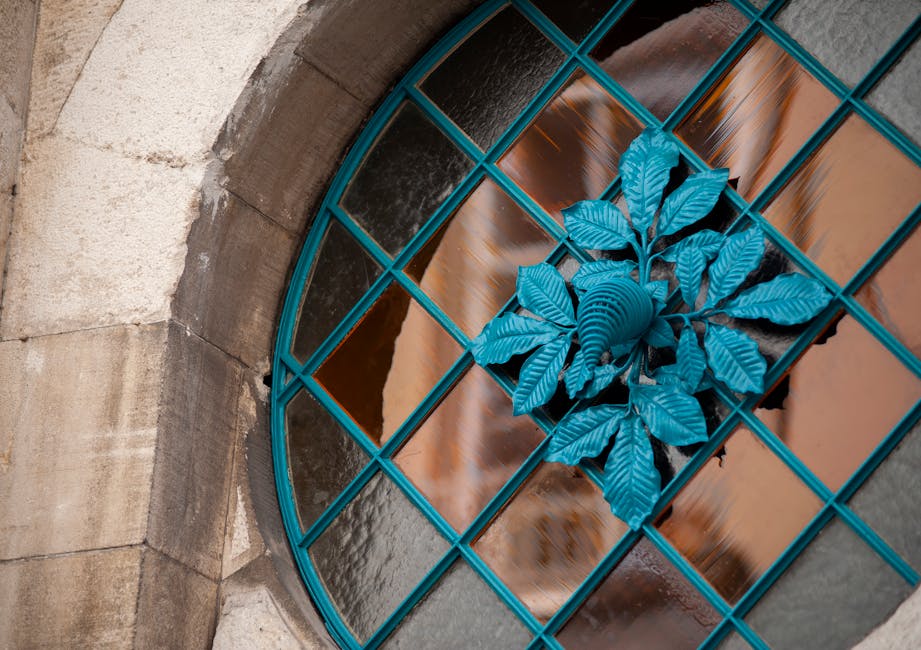 Close-up of a decorative stained glass window with a blue metallic leaf design, showcased in a kaleidoscope repeat pattern for wallpaper. — base photo: A detailed, close-up view of a decorative stained glass window, highlighting the metallic blue leaf 