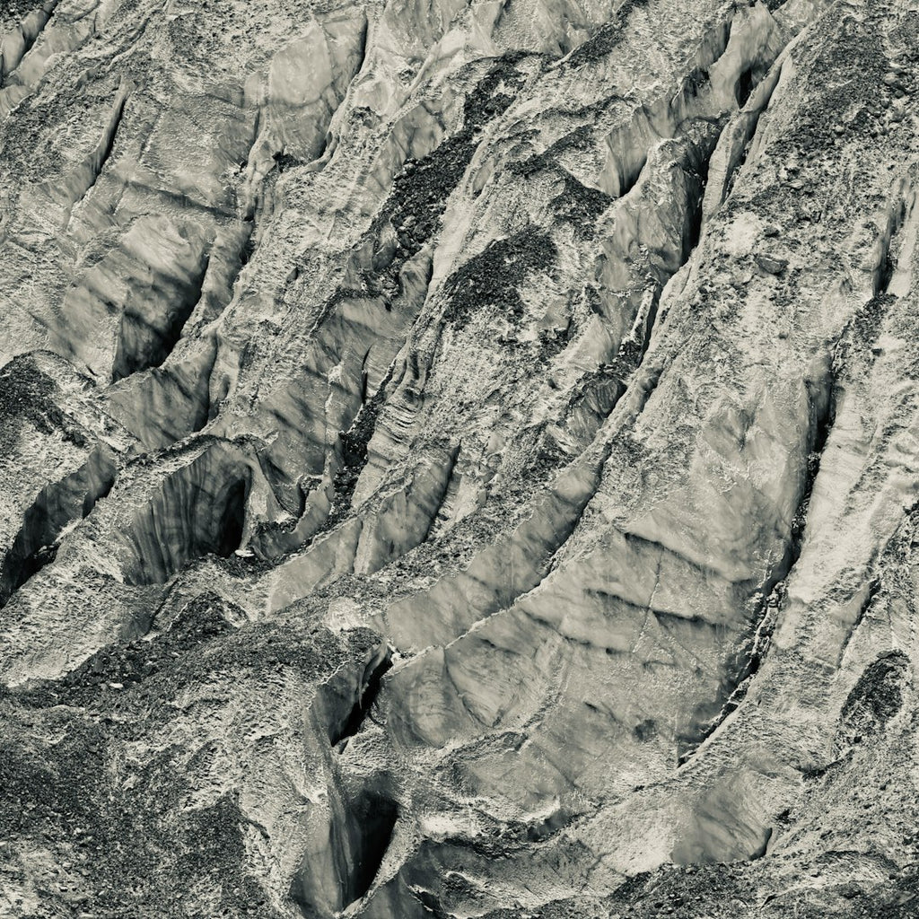 A seamless monochrome wallpaper pattern featuring kaleidoscopic reflections of a rocky mountain side with sharp contrast. — base photo: A stark, high-contrast black and white photograph by Danny Chen capturing the jagged rock formations