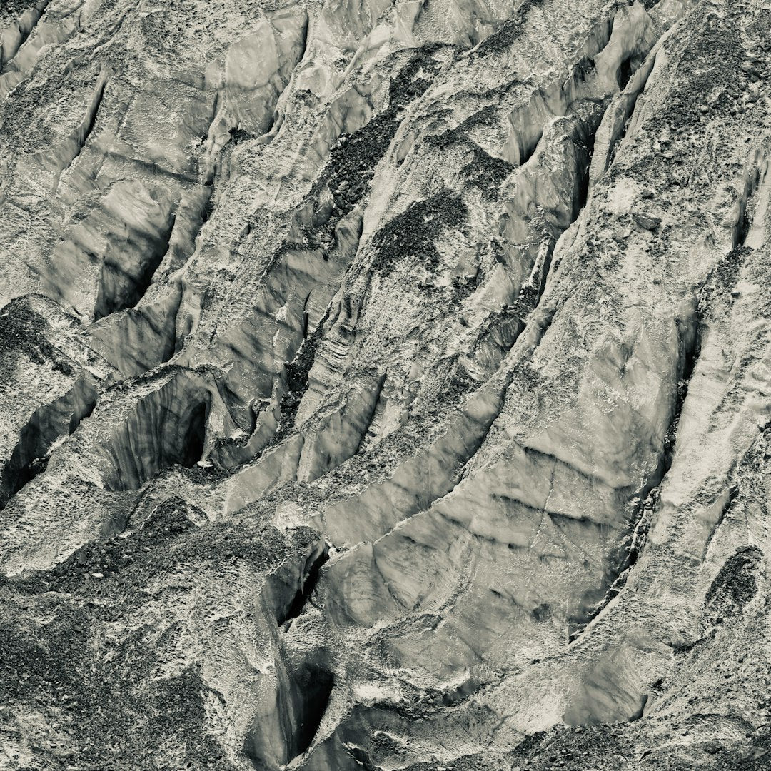 A seamless monochrome wallpaper pattern featuring kaleidoscopic reflections of a rocky mountain side with sharp contrast. — base photo: A stark, high-contrast black and white photograph by Danny Chen capturing the jagged rock formations