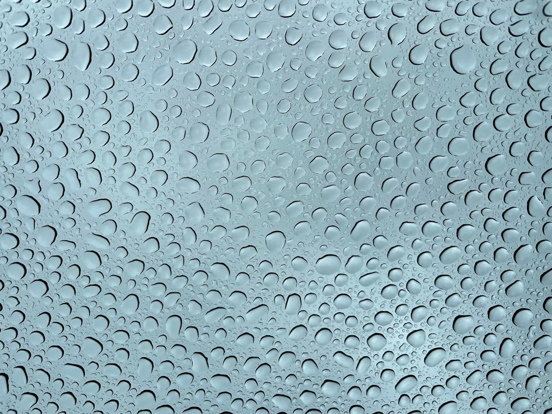 A symmetrical kaleidoscope pattern created from Borromean Rings, with a subtle texture of raindrops on glass, on wallpaper. — base photo: A close-up photograph of a windowpane covered in raindrops, where the water droplets distort and ref